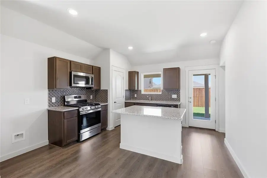 Kitchen featuring stainless steel appliances, tasteful backsplash, light stone countertops, vaulted ceiling, and recessed lighting