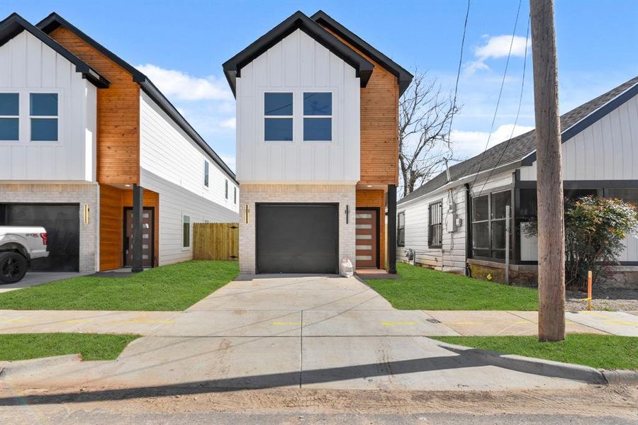 View of front of home featuring an attached garage, brick siding, concrete driveway, board and batten siding, and a front yard