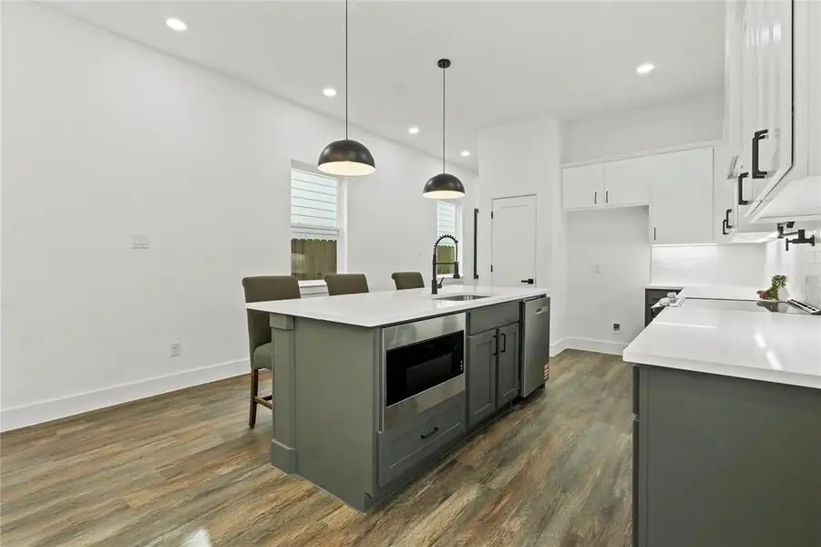 Kitchen featuring a kitchen bar, two tone cabinets, an island with sink, stainless steel appliances, and dark wood-type flooring