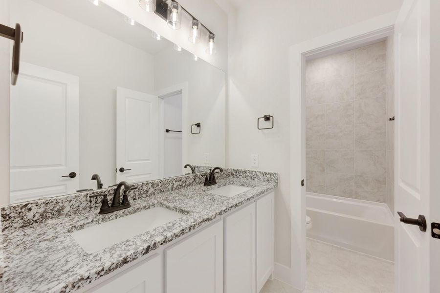 Bathroom with double sink vanity, granite countertops, white cabinets, and tiled shower-tub combo