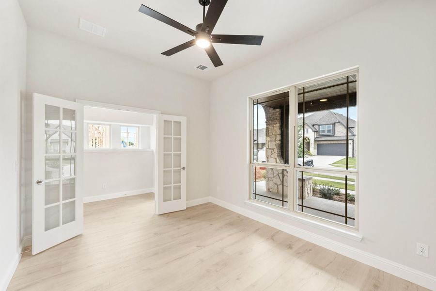 Empty room with light wood floors, ceiling fan, large window, and French doors leading to adjacent room