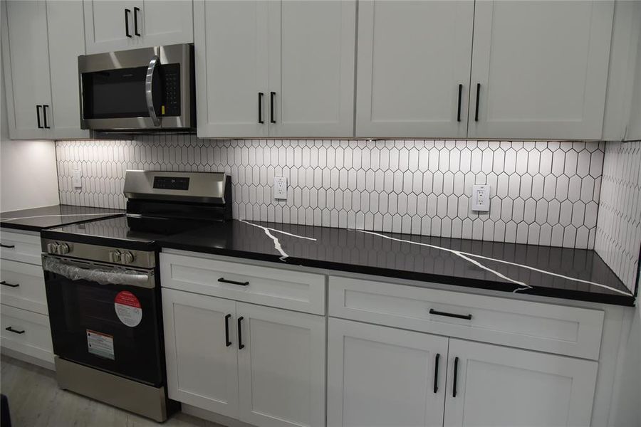 Kitchen featuring backsplash, white cabinets, stainless steel appliances, and light wood-type flooring