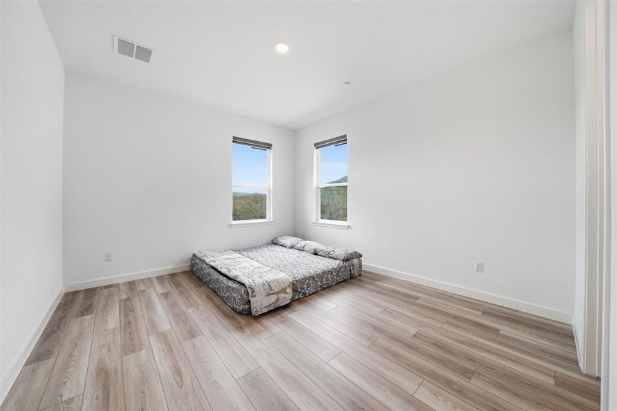This room features light-toned wood flooring, clean white walls, and two windows providing views of distant trees and hills