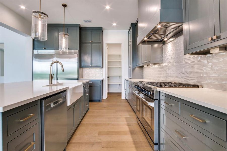 Kitchen with wall chimney exhaust hood, decorative backsplash, light countertops, and premium appliances