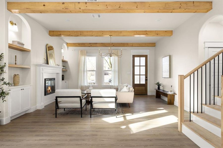 Living room featuring visible vents, a glass covered fireplace, light wood-style flooring, stairway, and beam ceiling