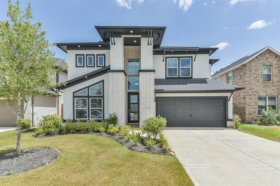 Modern two-story home with a mix of brick and stucco exterior, featuring large windows, a double-height entryway, and a two-car garage.