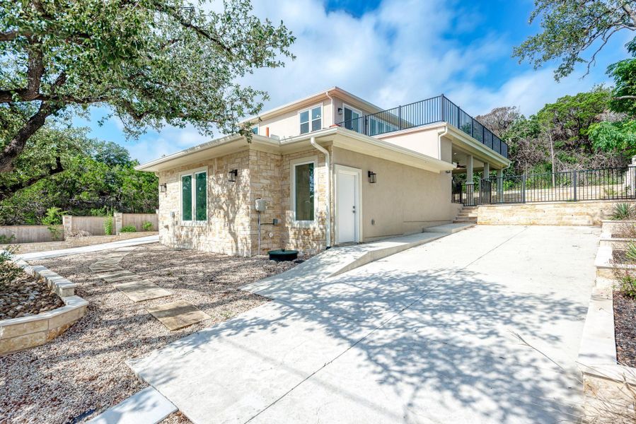 Back of property featuring stone siding, stucco siding, a balcony, and concrete driveway