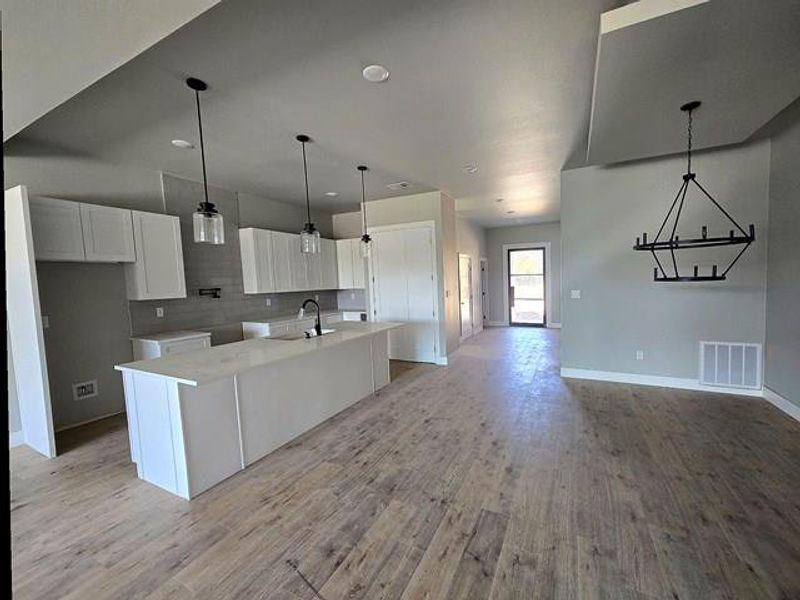 Kitchen with an island with sink, white cabinets, light wood-style flooring, a kitchen bar, and light stone counters