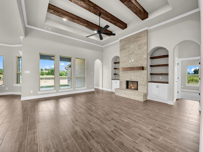 Unfurnished living room featuring arched walkways, wood finished floors, a fireplace, ceiling fan, and beamed ceiling Unfurnished living room featuring arched walkways, wood finished floors, a fireplace, ceiling fan, and beamed ceiling