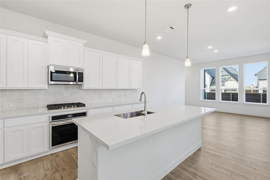 Kitchen with appliances with stainless steel finishes, white cabinets, an island with sink, hanging light fixtures, and backsplash