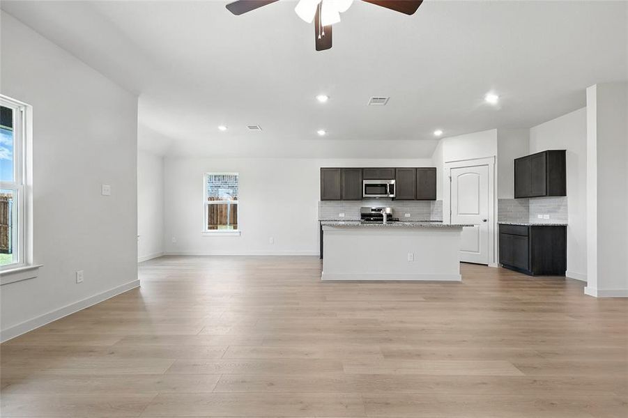 Kitchen with open floor plan, a kitchen island with sink, decorative backsplash, appliances with stainless steel finishes, and light wood finished floors Kitchen with open floor plan, a kitchen island with sink, decorative backsplash, appliances with stainless steel finishes, and light wood finished floors