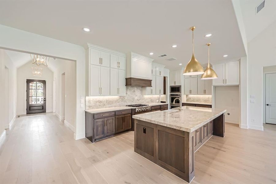 Kitchen with stainless steel appliances, hanging light fixtures, a center island with sink, and white cabinets