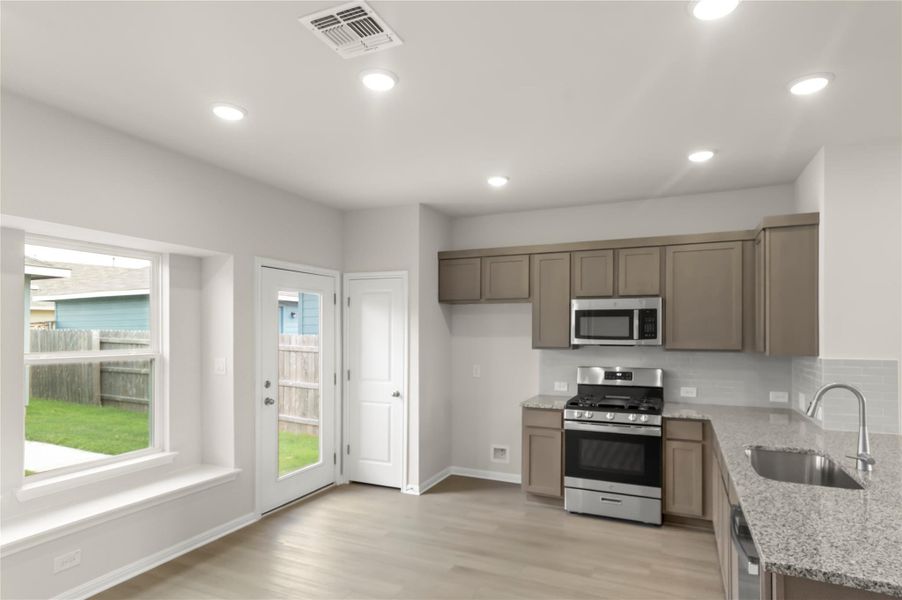 Kitchen featuring appliances with stainless steel finishes, light wood-type flooring, light stone counters, recessed lighting, and tasteful backsplash Kitchen featuring appliances with stainless steel finishes, light wood-type flooring, light stone counters, recessed lighting, and tasteful backsplash