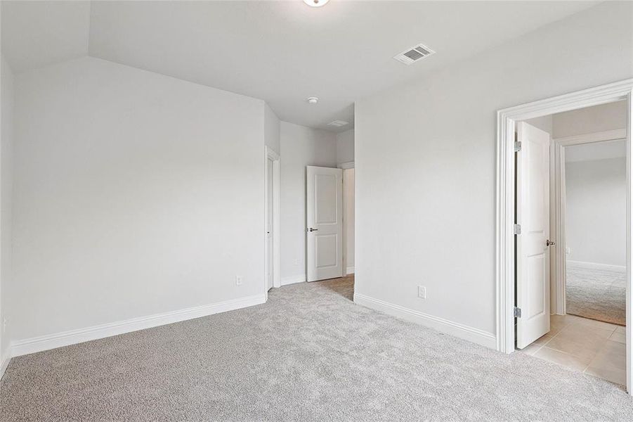 Unfurnished bedroom with vaulted ceiling and light colored carpet