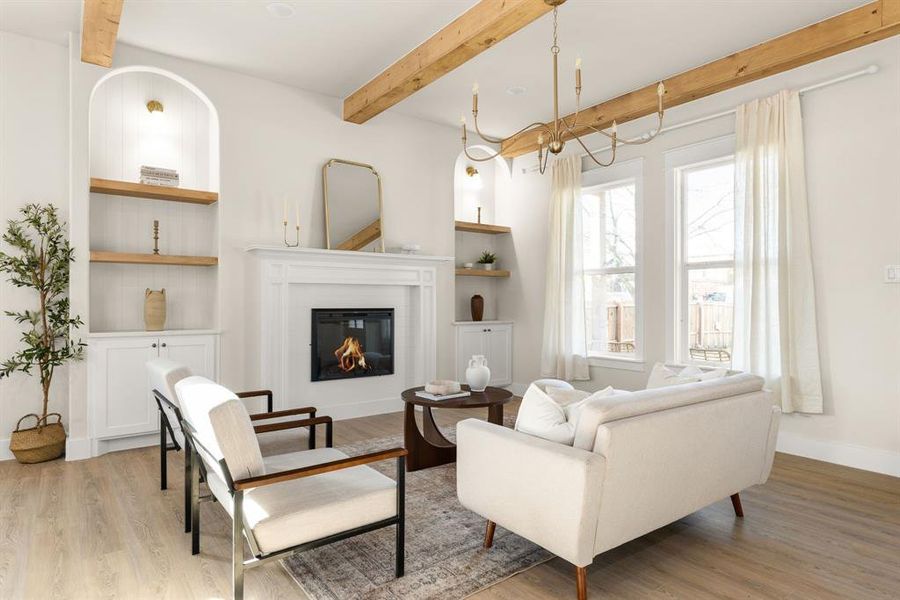 Living room featuring beam ceiling, baseboards, wood finished floors, and a glass covered fireplace