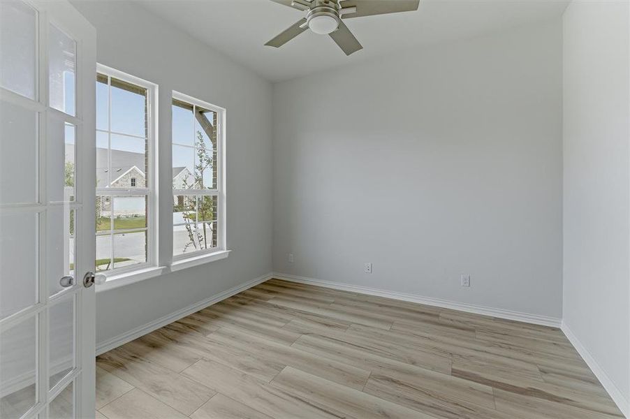 Room featuring wood-finish flooring, two large windows with grid patterns, and a ceiling fan with integrated lighting