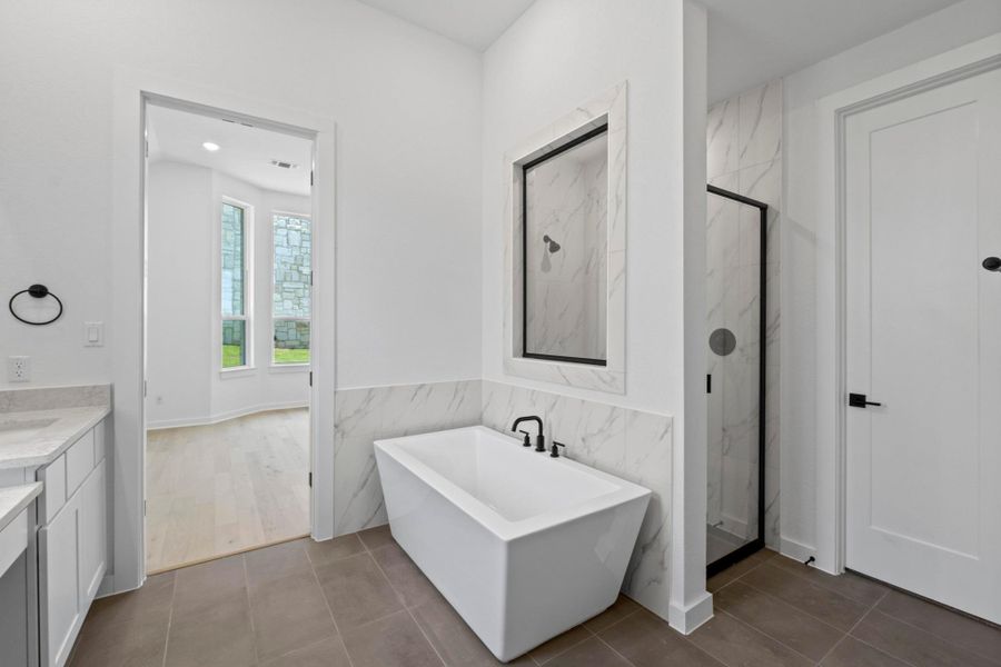 Bathroom featuring a marble finish shower, a freestanding bath, vanity, tile walls, and tile patterned flooring