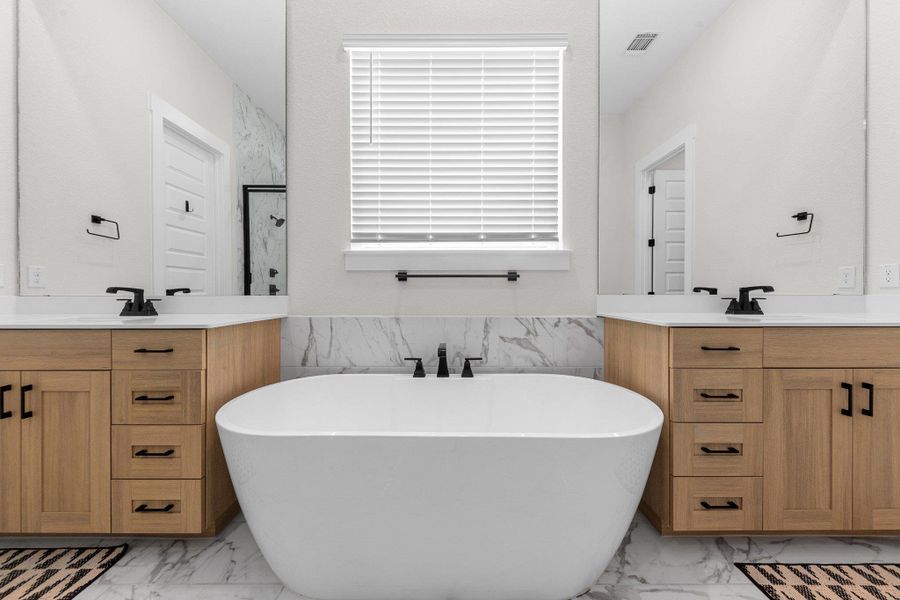 Bathroom with marble finish floor, a soaking tub, two vanities, visible vents, and a sink