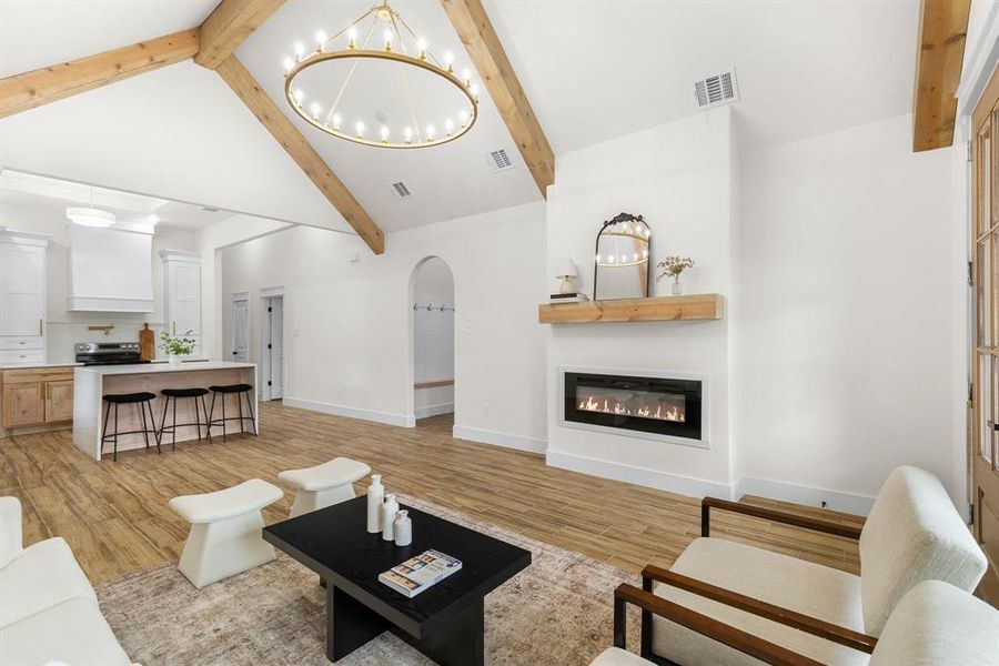 Living room with light hardwood / wood-style floors, an inviting chandelier, beam ceiling, and high vaulted ceiling