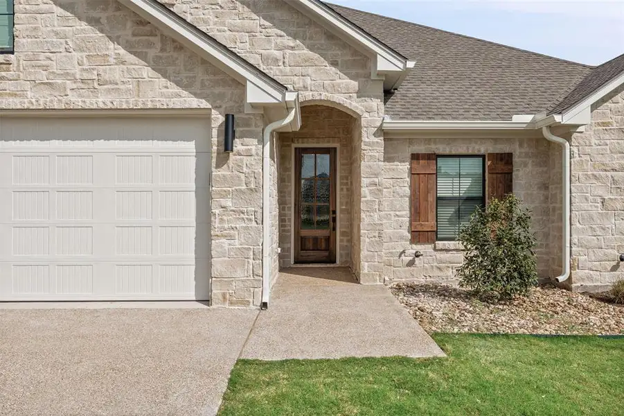 The property features an attractive stone exterior, a white panel garage door, and a dark wood entry door