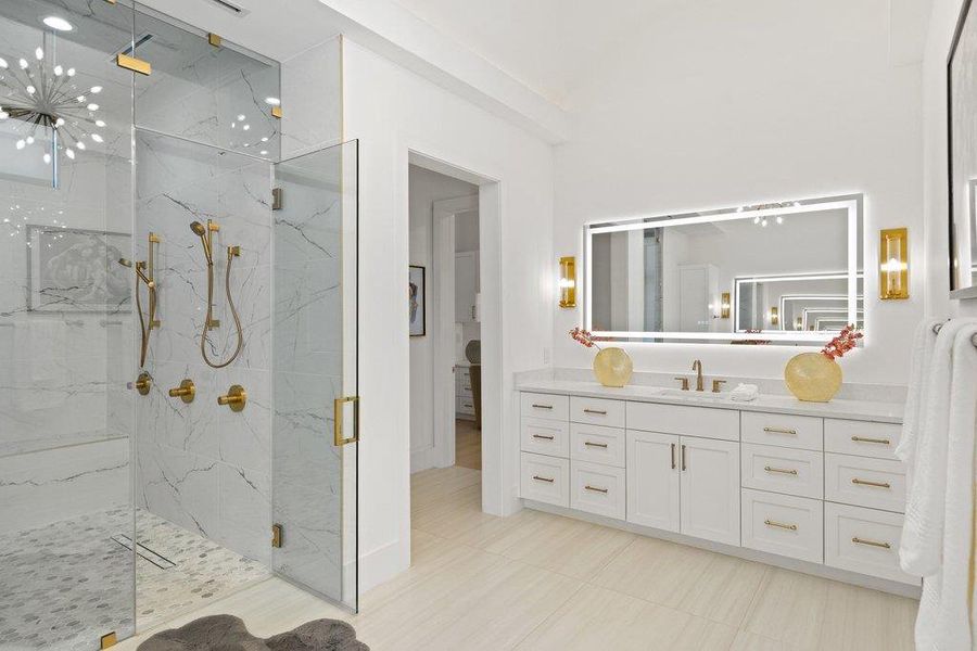 Modern bathroom featuring an illuminated vanity mirror and a spacious walk-in shower with elegant gold fixtures.