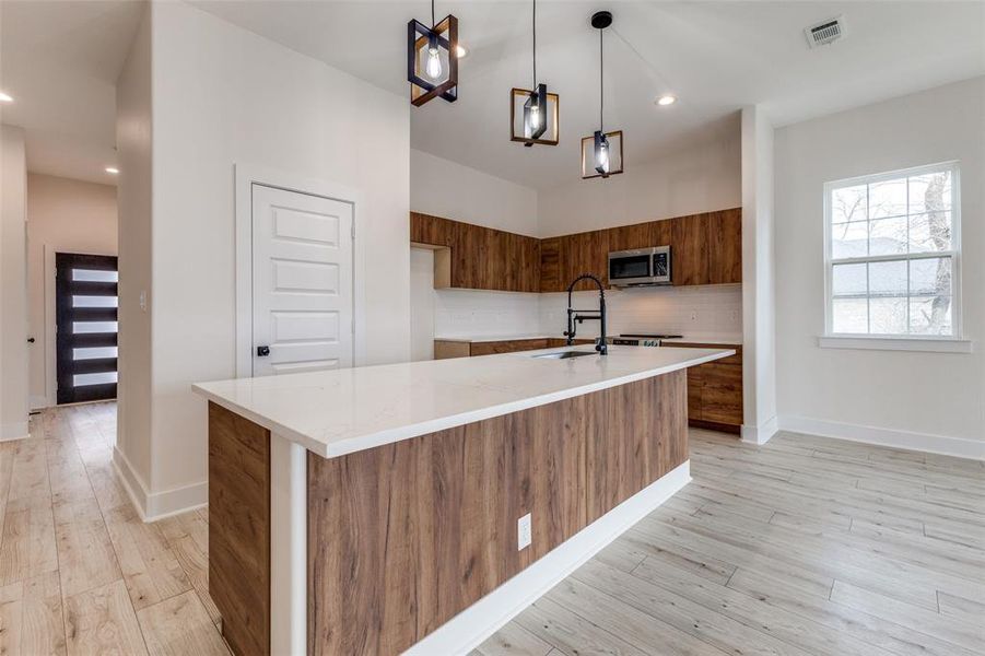 Kitchen with tasteful backsplash, stainless steel microwave, visible vents, brown cabinets, and modern cabinets