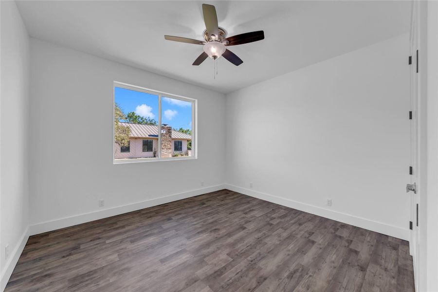 Guest Bedroom 2; Rich wood floors and clean white walls frame a bright window framing blue sky views.