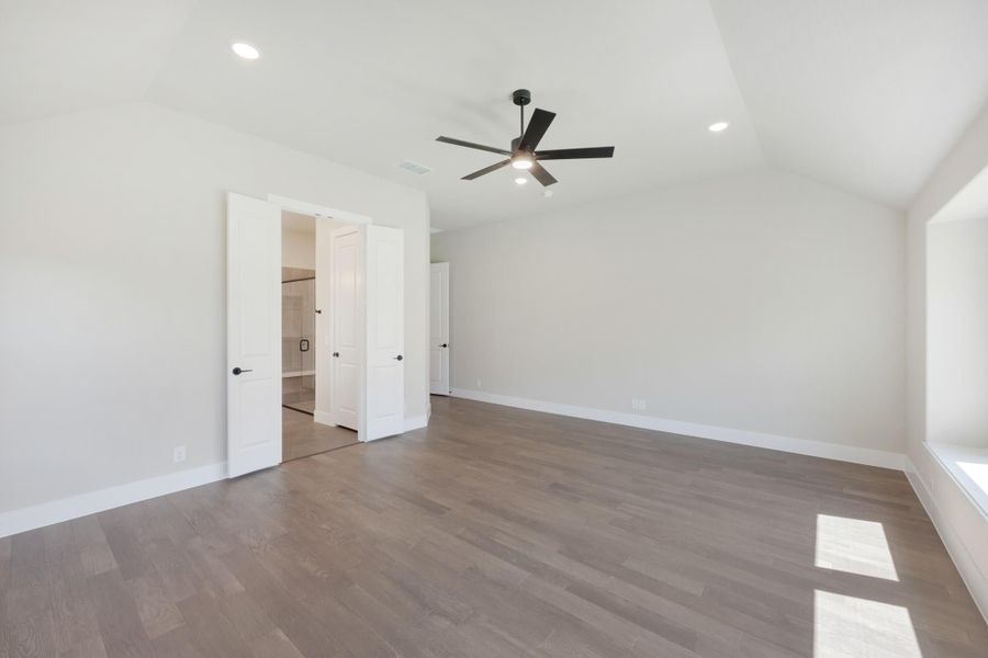 Empty master bedroom with hardwood floors, ceiling fan, and open door to ensuite bathroom