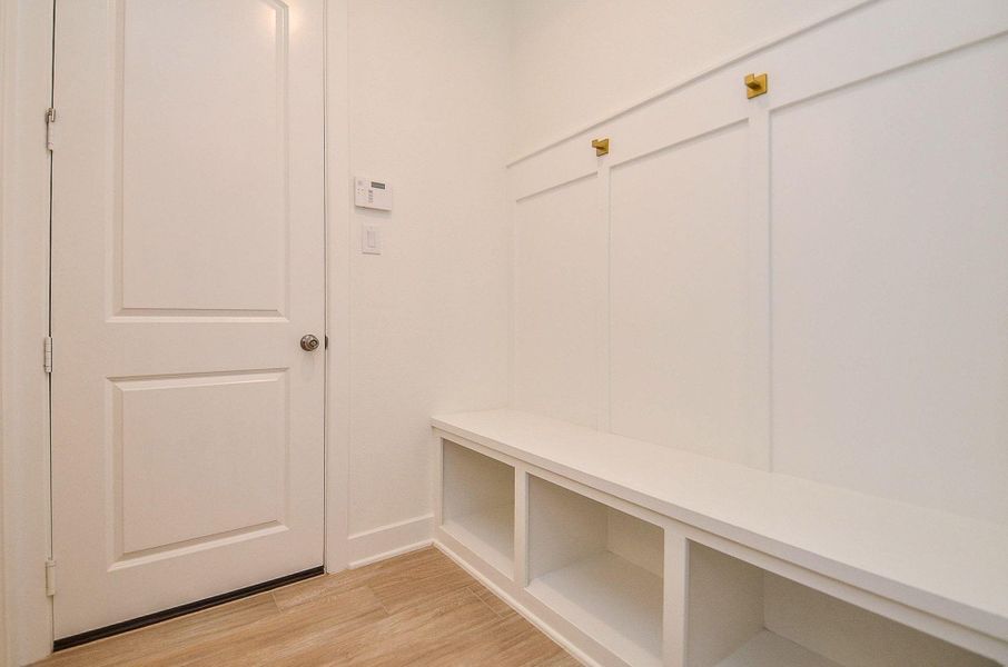 Built-in mudroom bench with wainscot paneling, brushed-gold coat hooks, and entry from the garage.