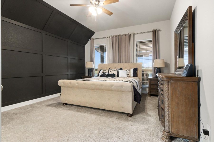 This bedroom features a striking dark accent wall. It has soft carpeting, large windows with curtains, and a ceiling fan. Space for all of your bedroom furniture and more.