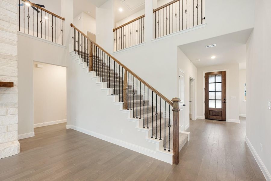 Two-story foyer with carpeted staircase, wood and iron balusters, hardwood floors, and wood front door with glass panels Two-story foyer with carpeted staircase, wood and iron balusters, hardwood floors, and wood front door with glass panels