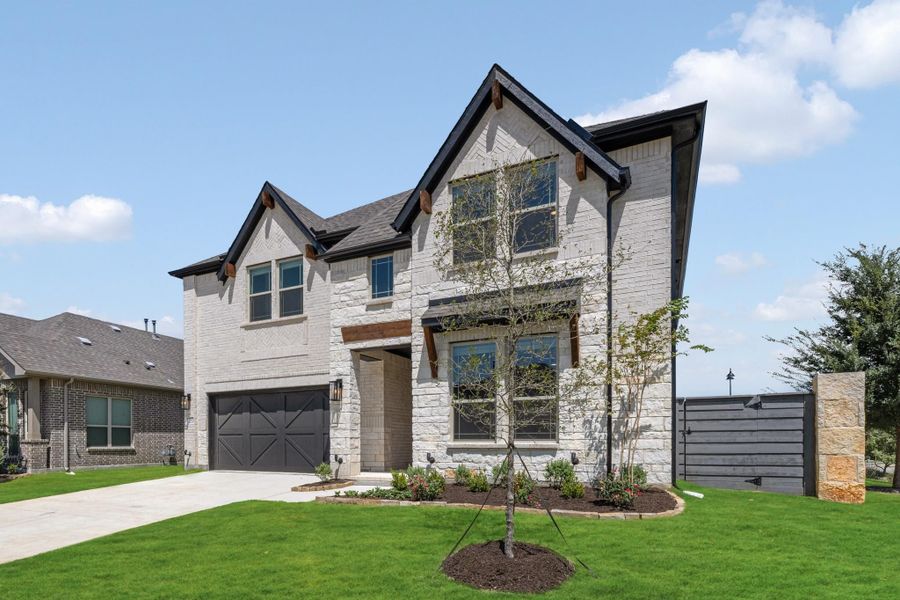 Two-story home with white stone exterior, dark two-car garage, wood accents, and manicured front lawn