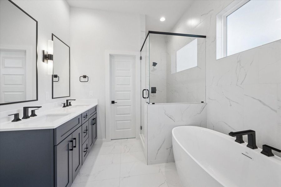 Luxurious primary bathroom at Thornton Oaks featuring a modern double vanity with dark cabinetry, elegant quartz countertops, and chic matte black hardware. This spa-inspired space includes a deep freestanding soaking tub, a frameless glass walk-in shower with designer marble-pattern tile, and contemporary lighting, perfect for a new construction home near Oak Forest.