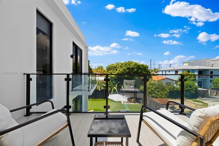 Second-story balcony featuring light-toned composite decking and a black-framed glass railing