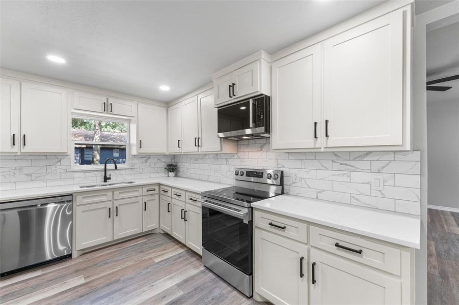 Modern kitchen featuring white shaker cabinetry, stainless steel appliances, white subway tile backsplash, light wood-finish flooring, and recessed lighting Modern kitchen featuring white shaker cabinetry, stainless steel appliances, white subway tile backsplash, light wood-finish flooring, and recessed lighting