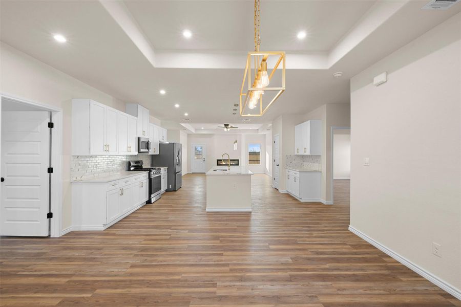 Kitchen with a raised ceiling, backsplash, white cabinetry, and recessed lighting Kitchen with a raised ceiling, backsplash, white cabinetry, and recessed lighting