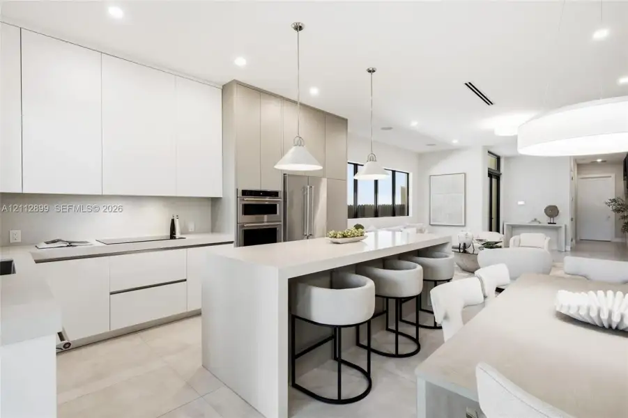 Kitchen featuring floor-to-ceiling cabinetry, a waterfall-edge center island, stone countertops, recessed lighting, and stainless steel built-in double wall ovens