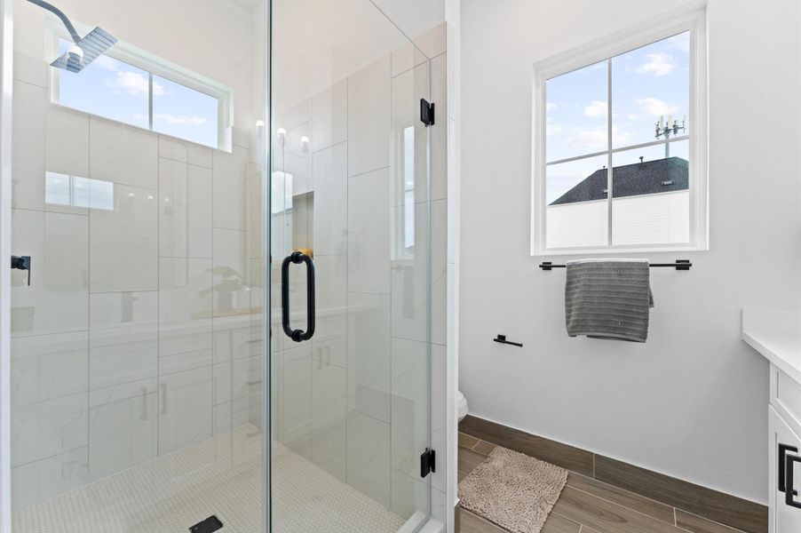 This elegant primary bathroom features a sleek double-sink vanity topped with quartz countertops, offering both style and functionality. The spacious layout includes a glass-enclosed walk-in shower, accented with modern tilework and premium fixtures.