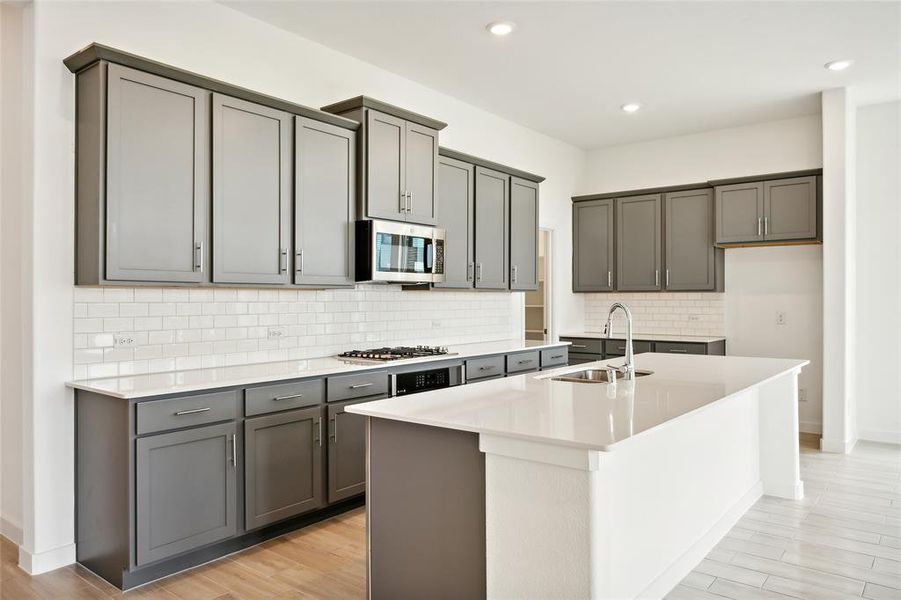 Kitchen featuring a center island with sink, stainless steel appliances, sink, and gray cabinetry