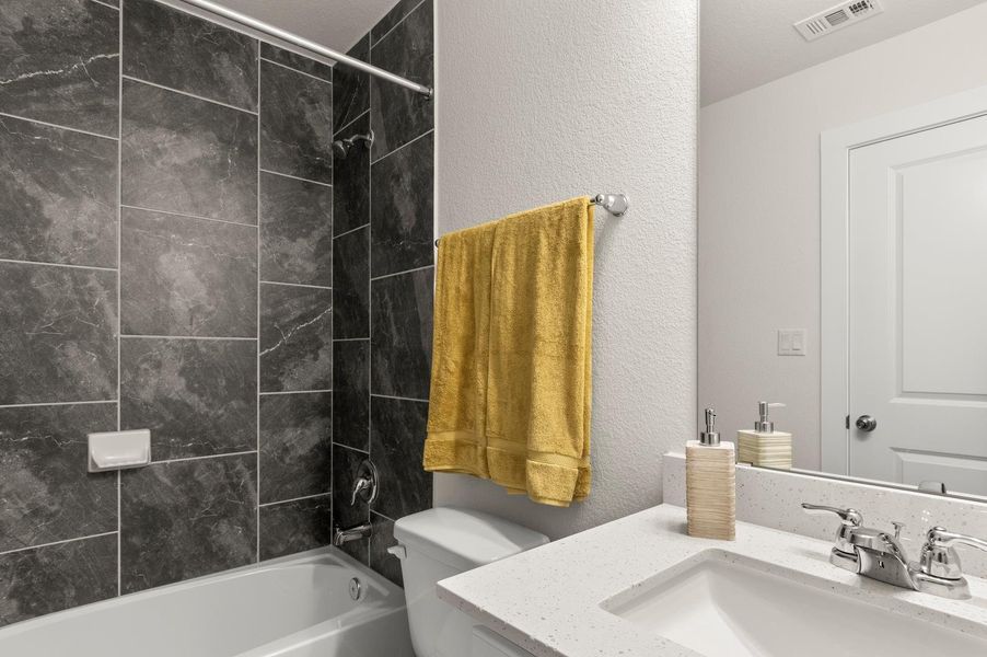 A refined bathroom features a shower-tub combo with dark tiled walls and a bright white vanity with a sleek countertop.