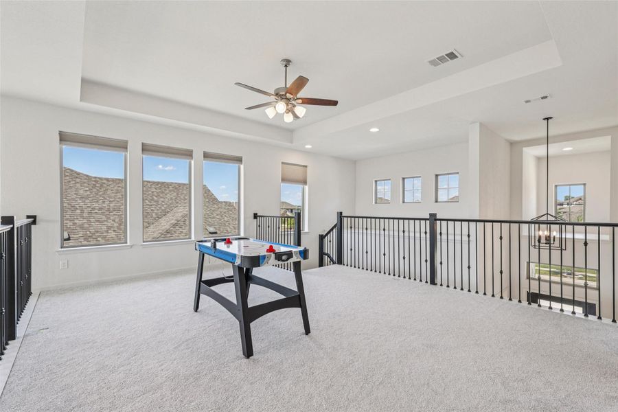 Expansive loft area featuring light-colored carpeting, multiple windows providing natural light, and a ceiling fan