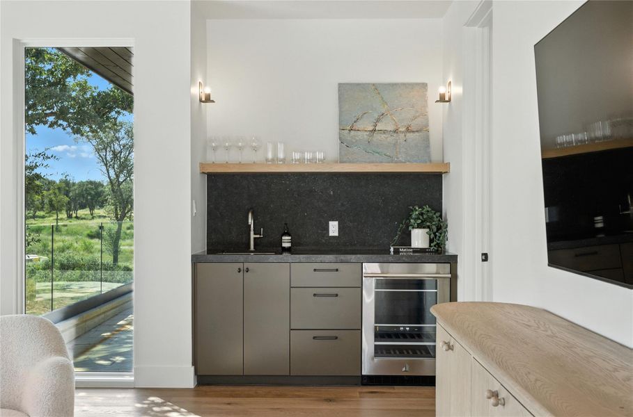 Indoor wet bar with open shelves, wine cooler, light wood-style flooring, gray cabinets, and tasteful backsplash