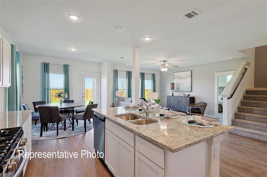 Open-concept living area featuring a kitchen island with dual sinks and stone countertops, wood-finish flooring, recessed lighting, and a staircase with a dark wood handrail
