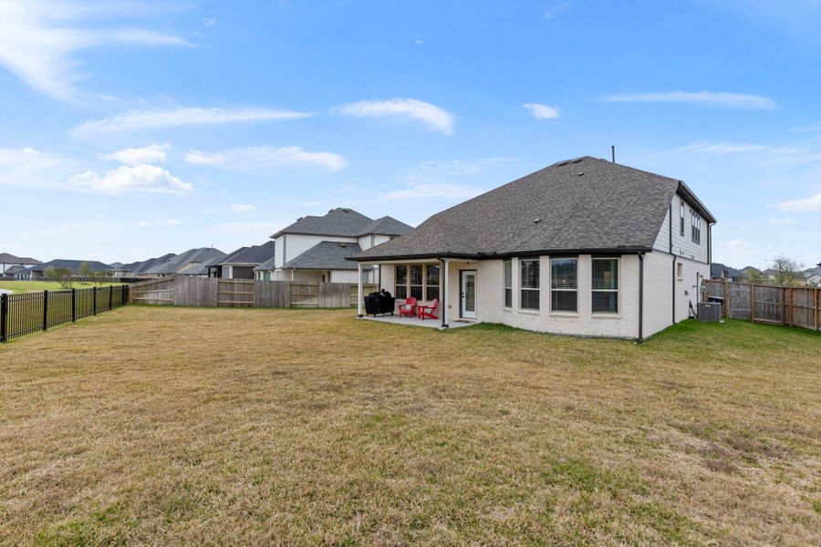 Spacious backyard with a covered patio, perfect for outdoor gatherings. The yard is fenced, providing privacy and security, and the house features large windows for ample natural light.