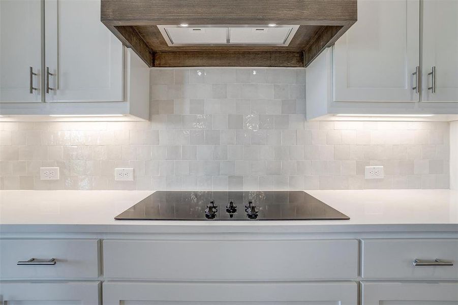 Kitchen featuring premium range hood, black electric stovetop, white cabinetry, and decorative backsplash