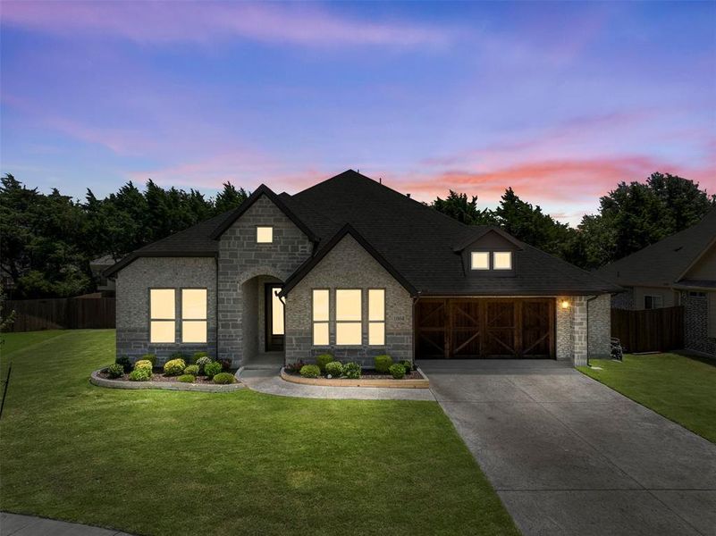 Stone facade home with a black shingle roof and a two-car garage featuring a dark wood-finish door Stone facade home with a black shingle roof and a two-car garage featuring a dark wood-finish door