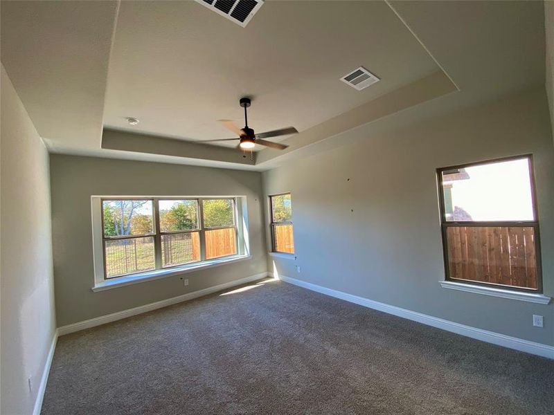 Large master bedroom with tray ceiling, window seat, and ceiling fan