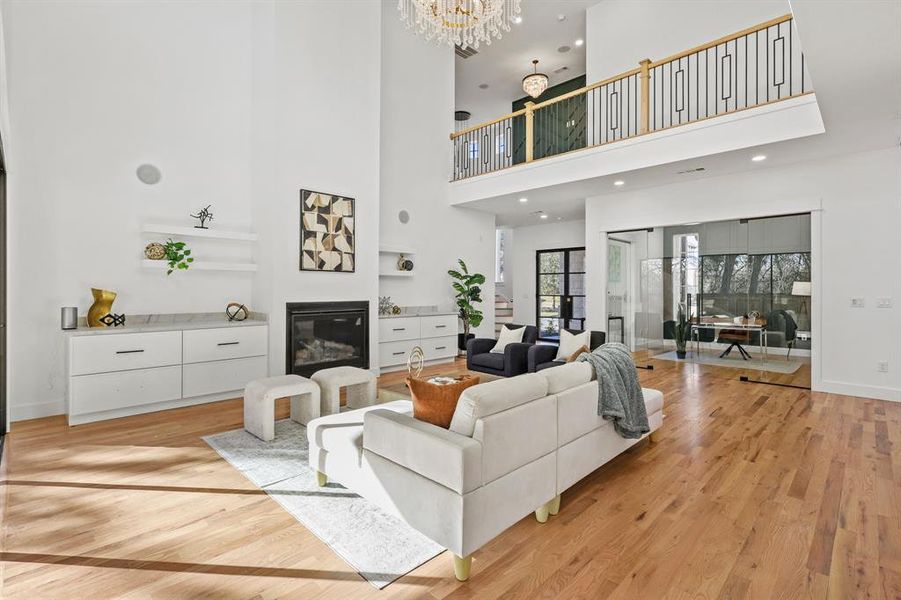 Living room with light hardwood / wood-style flooring, a towering ceiling, and an inviting chandelier