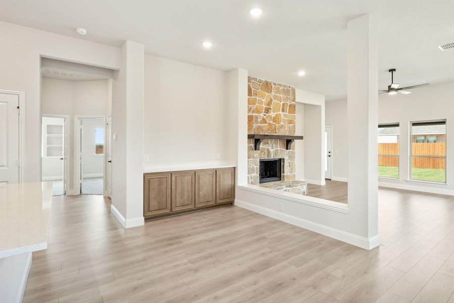 Open living area with stone fireplace, wood cabinets, and light hardwood floors Open living area with stone fireplace, wood cabinets, and light hardwood floors