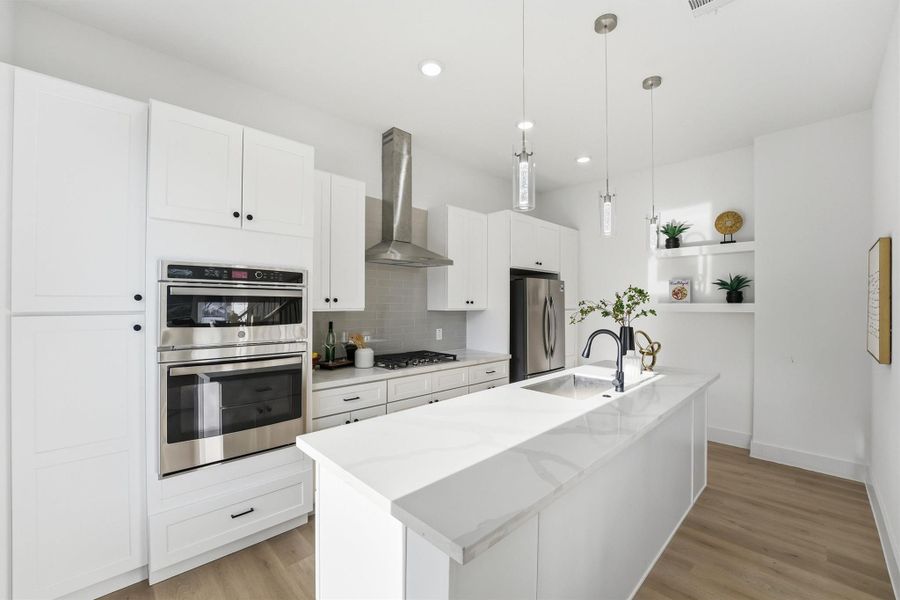 Spacious, modern kitchen featuring white shaker cabinetry, quartz countertops, built-in double ovens, stainless steel appliances, pendant lighting, and a large waterfall island designed for effortless entertaining and everyday functionality.